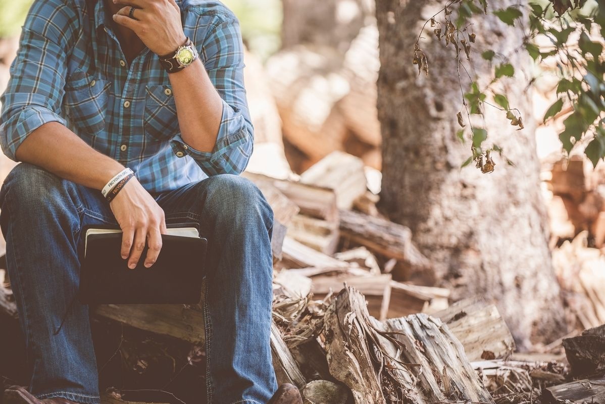 A man holding a notebook sitting in the woods